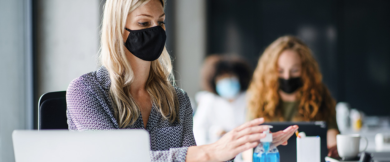masked employee using hand sanitizer at work