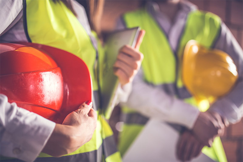 close up of two workers wearing safety vests and holding hard hats