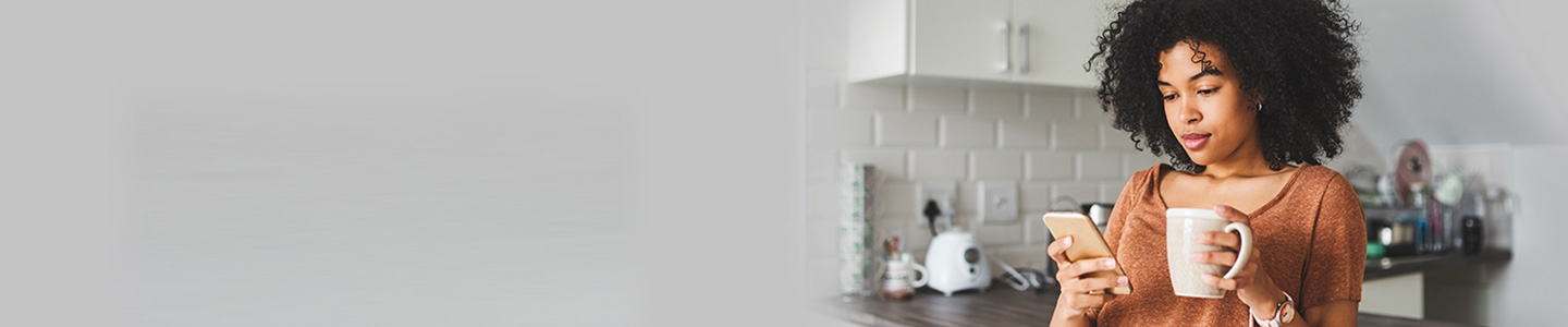 woman holding mug and looking at mobile phone