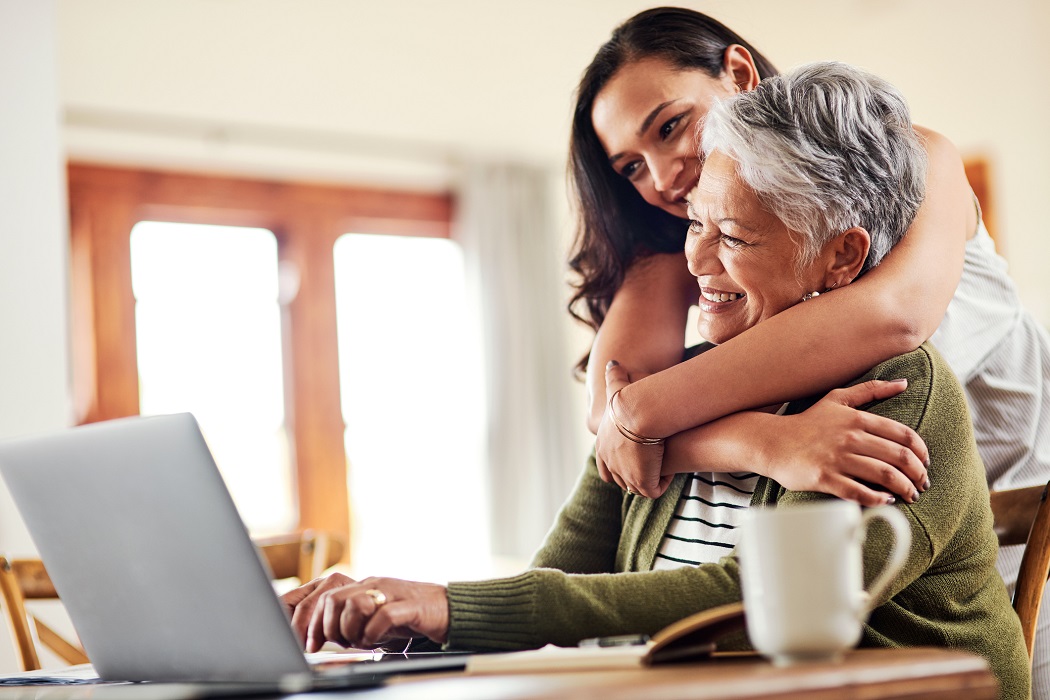 a young woman hugs an older woman while looking at a laptop