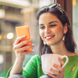 woman holding mug and looking at mobile phone