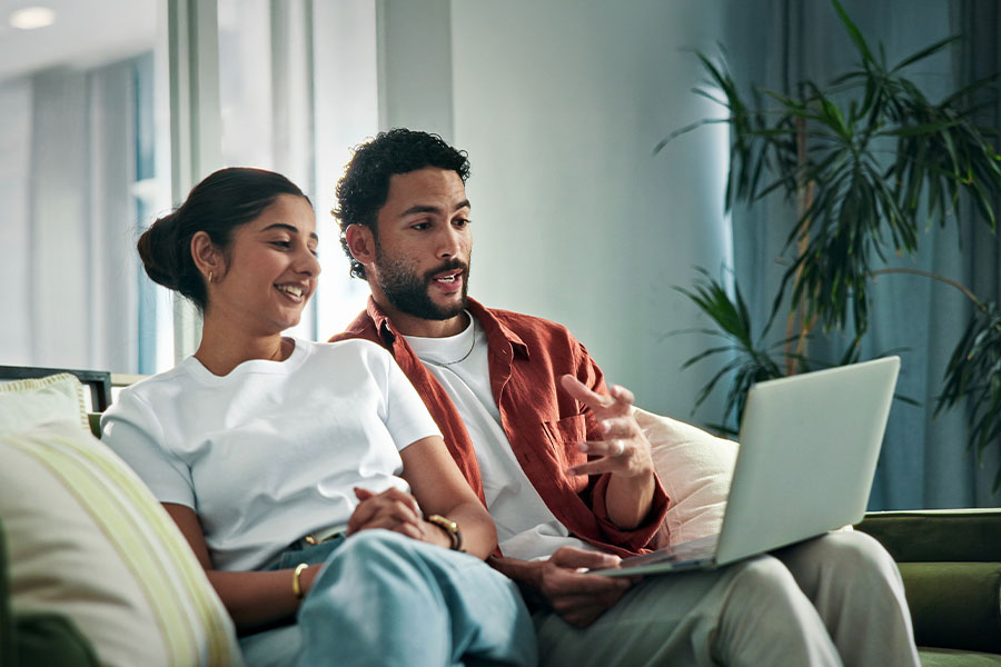 couple sitting on couch looking at laptop computer