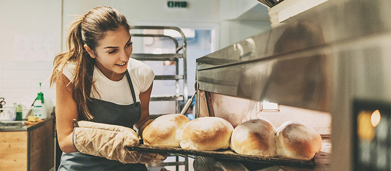 woman getting freshly baked loaves of bread out of an electric combination-oven